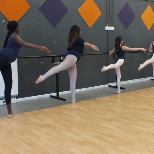 5 dancers at the barre in arabesque grand battement